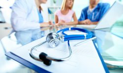 Close-up of stethoscope and paper on background of doctors and patient working with laptop