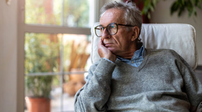 Senior white man looking out of window at home